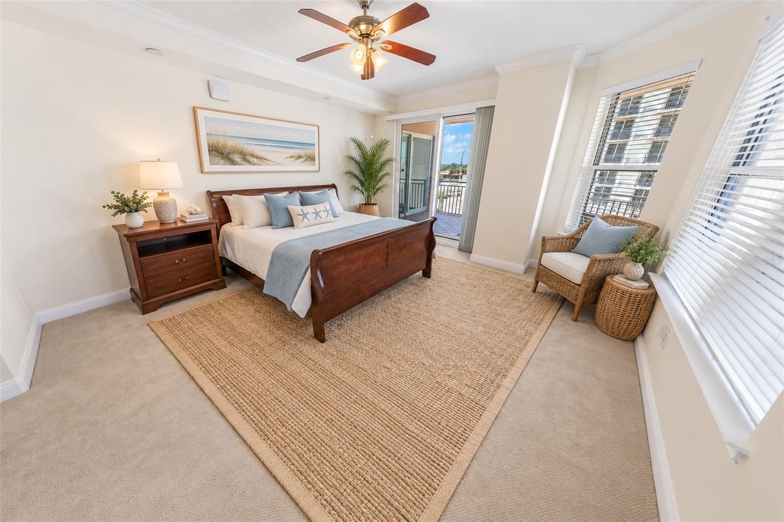 Staged bedroom with a dark wood bed, woven rug, and sliding glass door to a balcony.