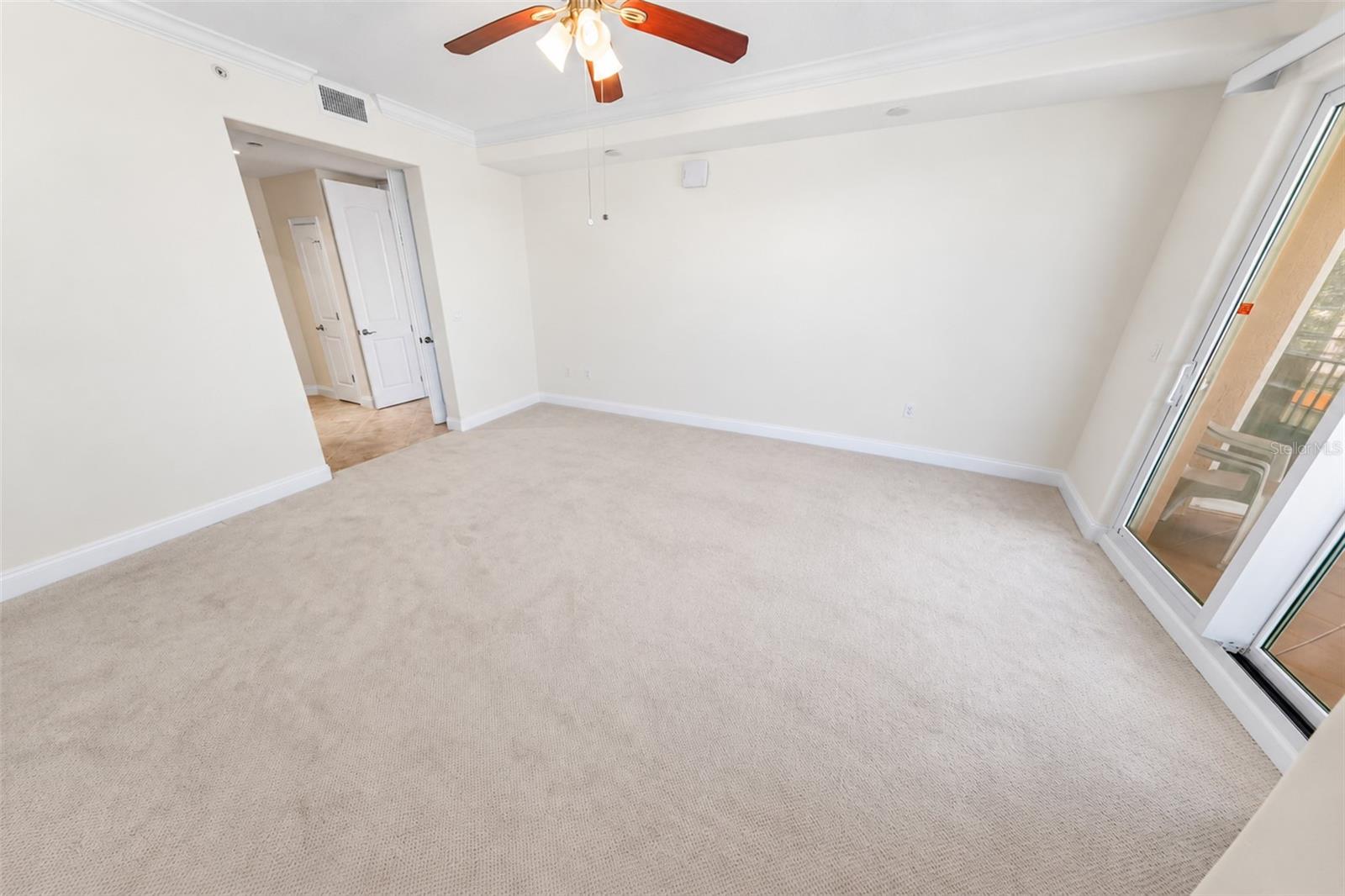 Empty carpeted living room with a ceiling fan and sliding glass doors to a balcony.
