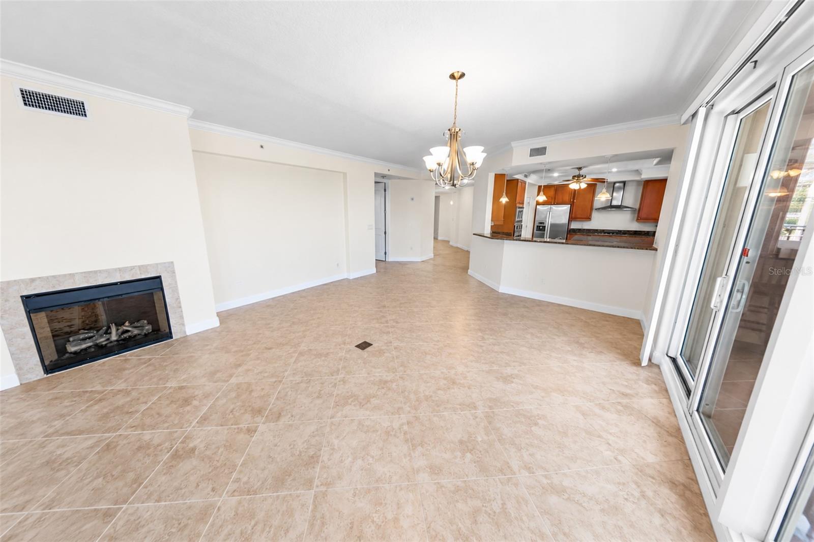 Vacant condo living area with tile floors, a fireplace, and an open kitchen.
