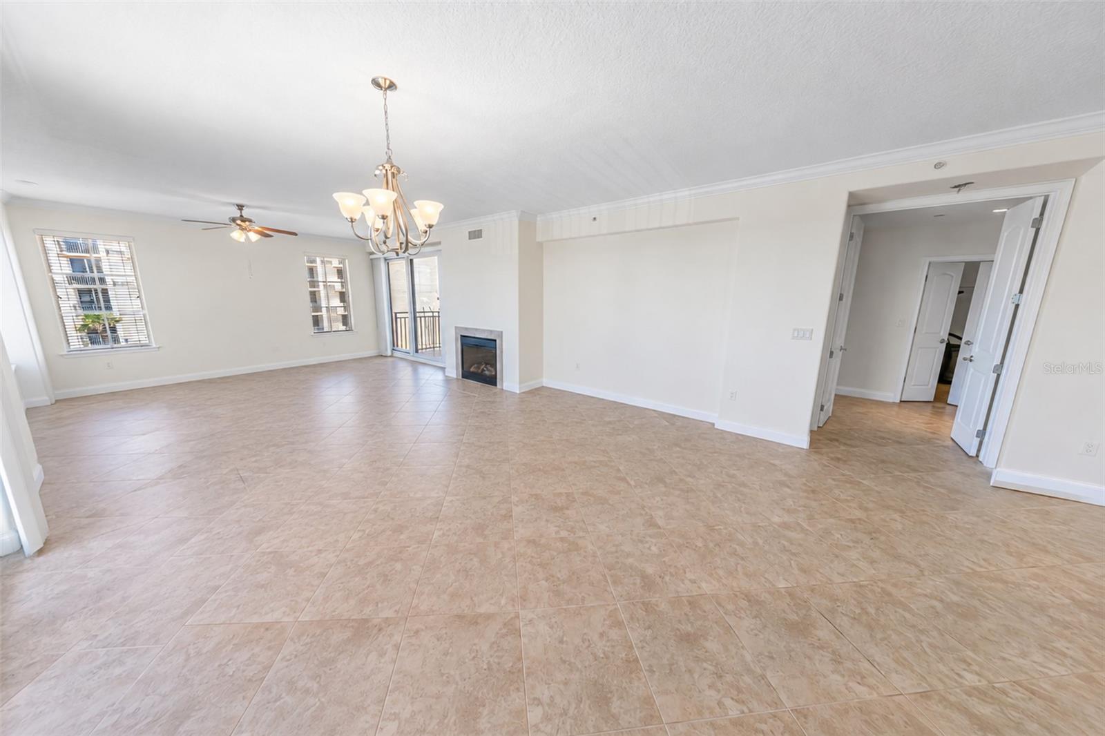 Empty living and dining area with beige tile floors, a fireplace, and balcony access.