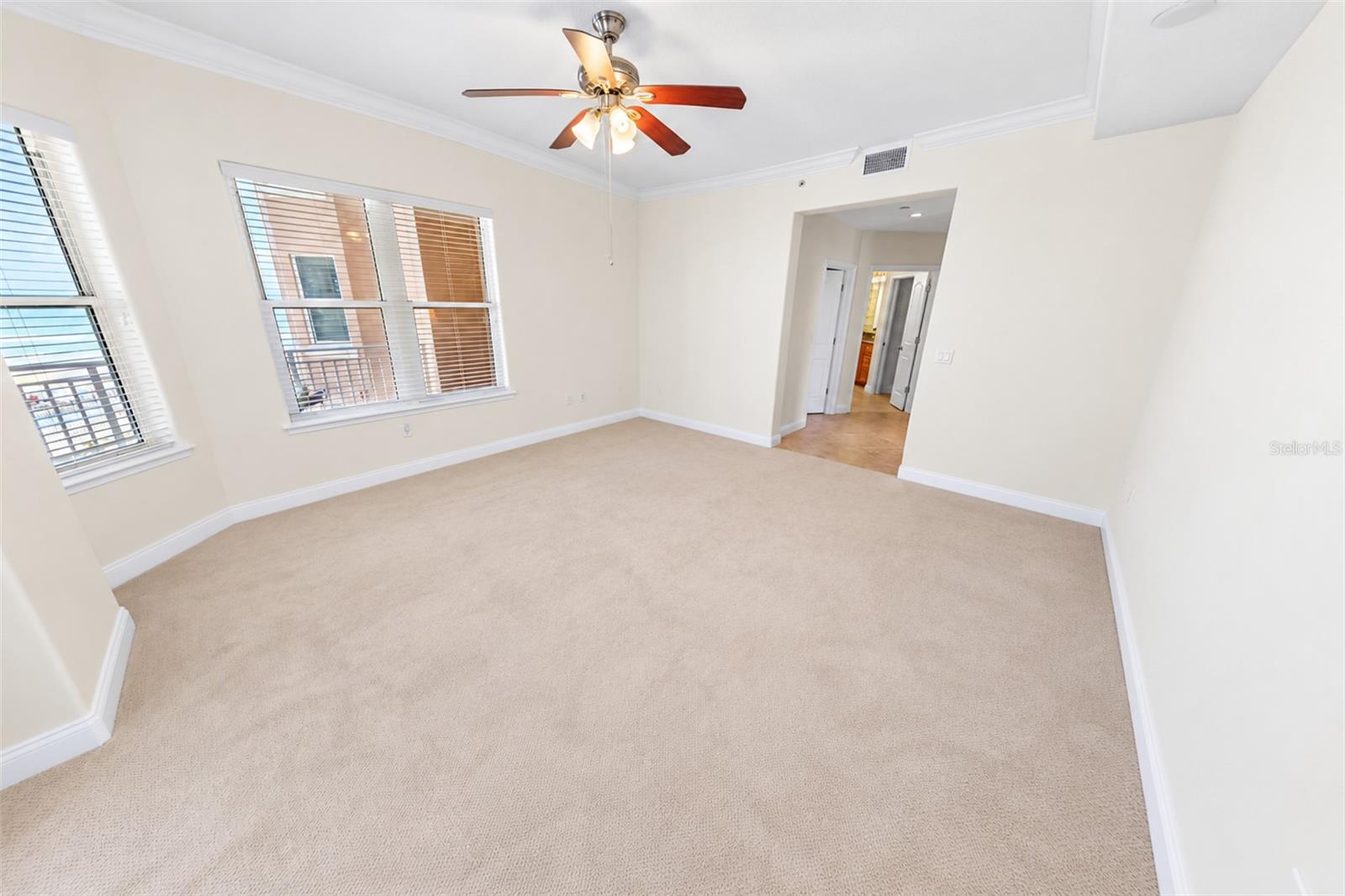 Empty carpeted bedroom with two windows, white blinds, and a ceiling fan.