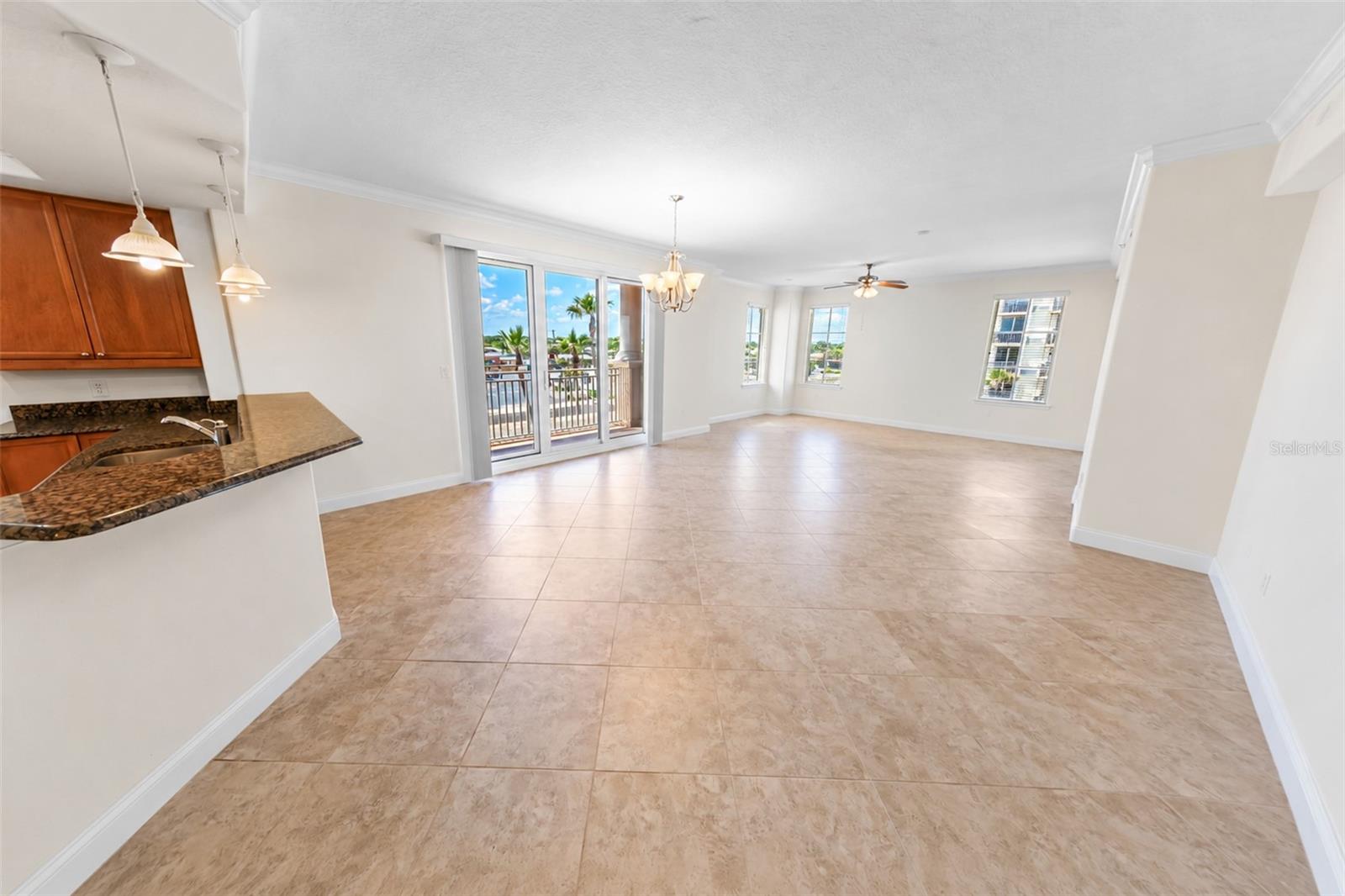 Unfurnished condo living and dining area with tiled floors, kitchen peninsula, and sliding doors to a balcony.