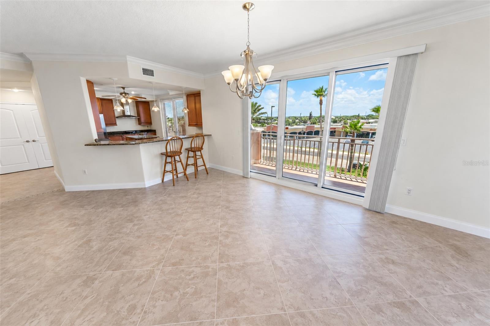 Dining area with tiled floors, kitchen breakfast bar, and sliding doors to a sunny balcony.