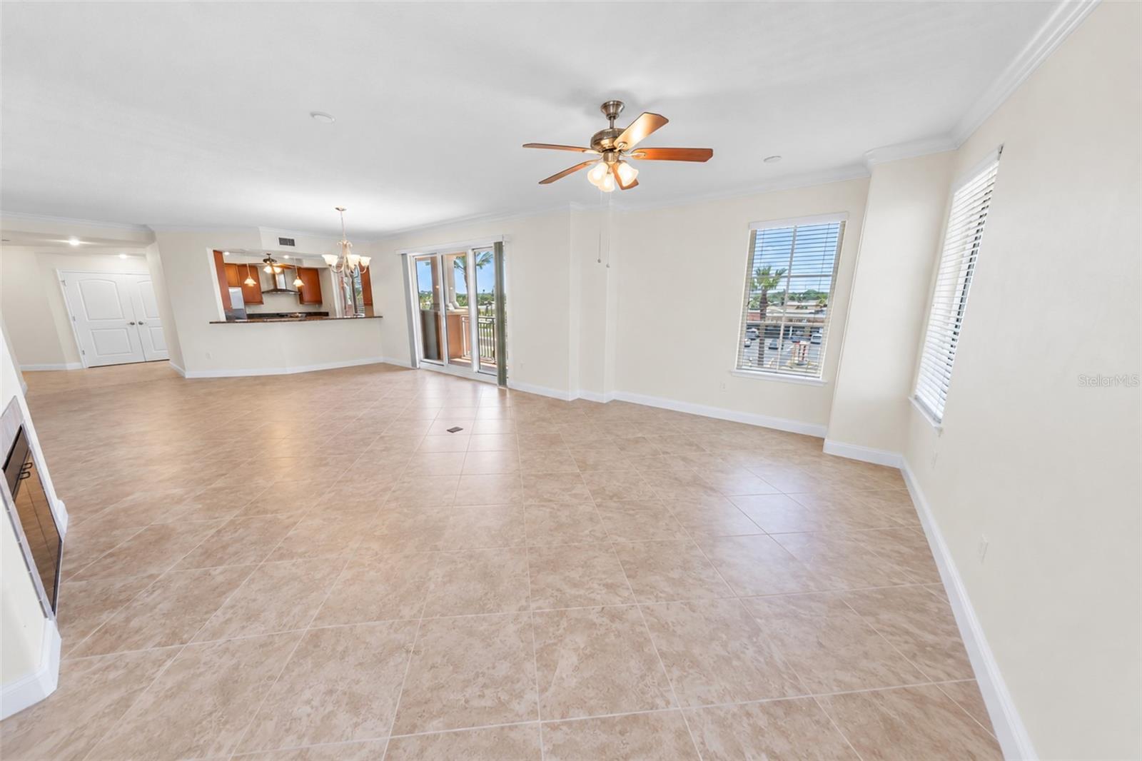 Unfurnished condo living area with beige tile floors, a ceiling fan, and sliding glass doors to a balcony.