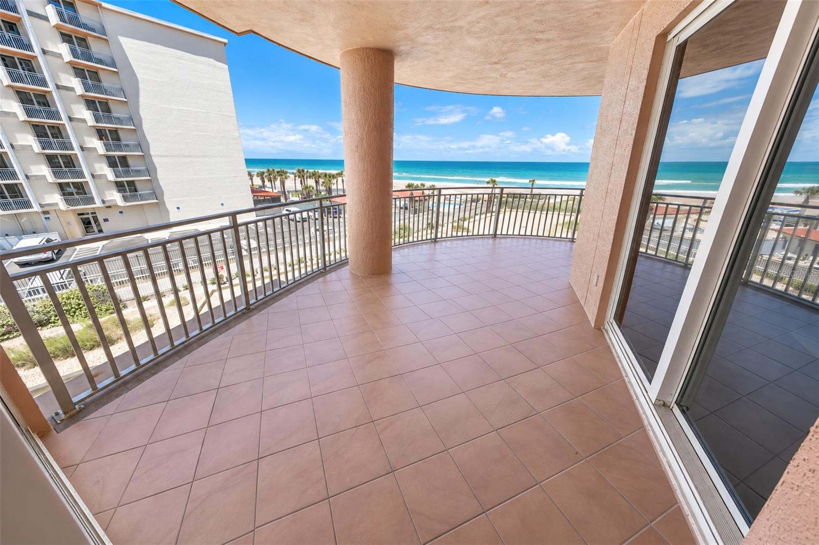 Ocean-view condo balcony with tiled floor, metal railings, and a round column.