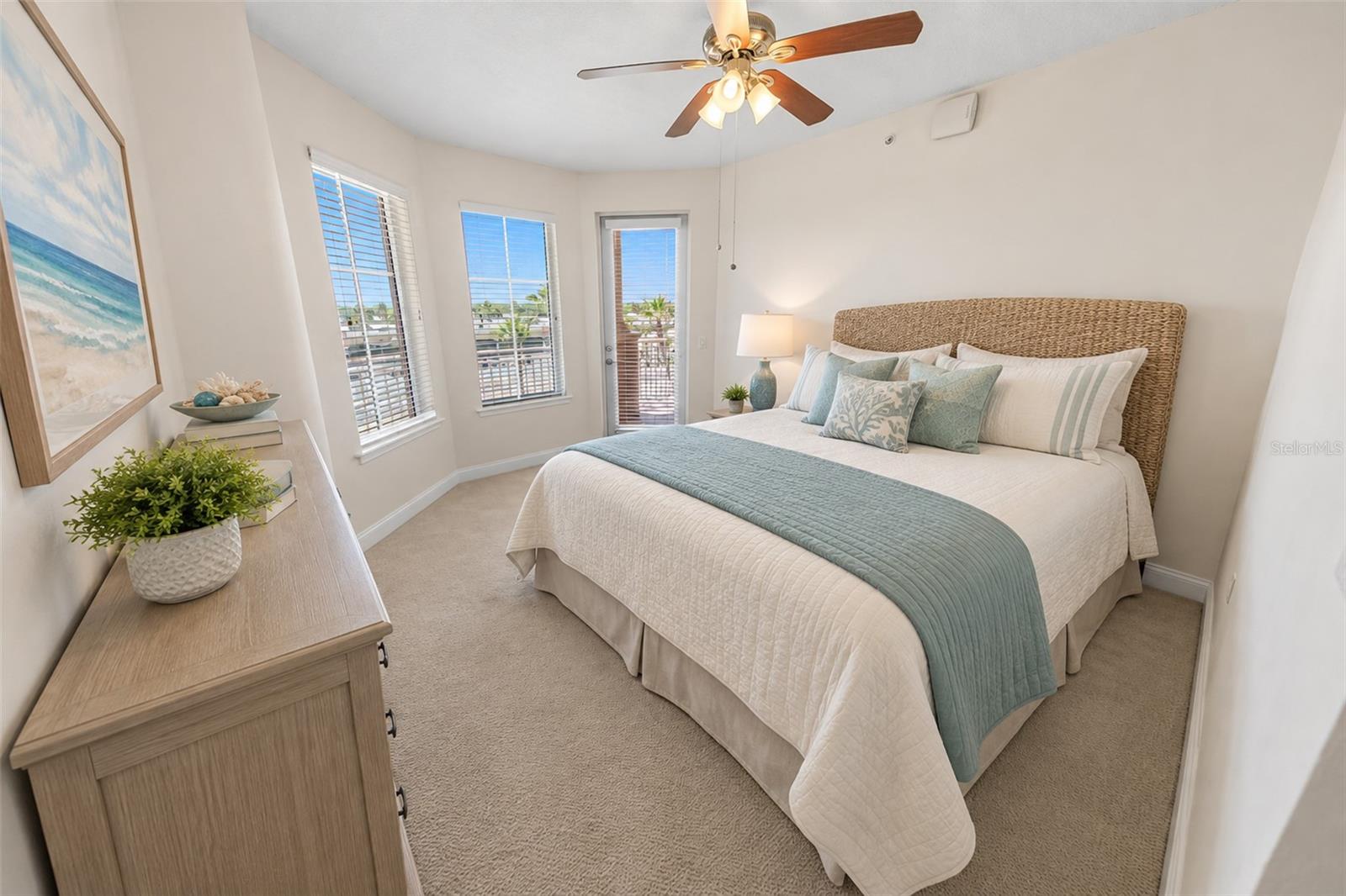 Bedroom with a woven-headboard bed, pale aqua bedding, and windows beside a balcony door.