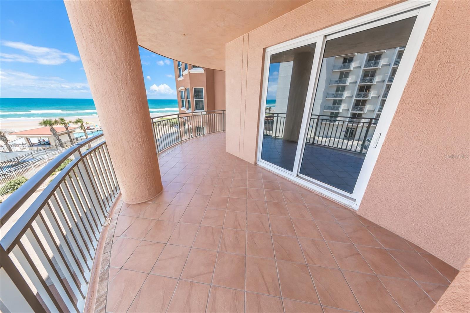 Condominium balcony overlooking the beach and ocean, with terracotta tile, metal railings, and a large stucco column.