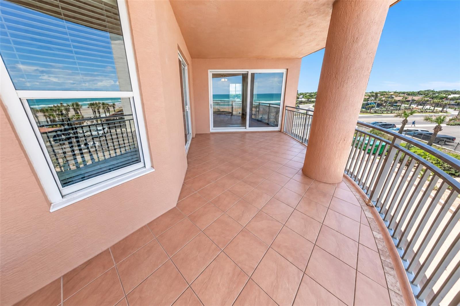 Covered tiled condo balcony overlooking the ocean, with metal railings and a large column.