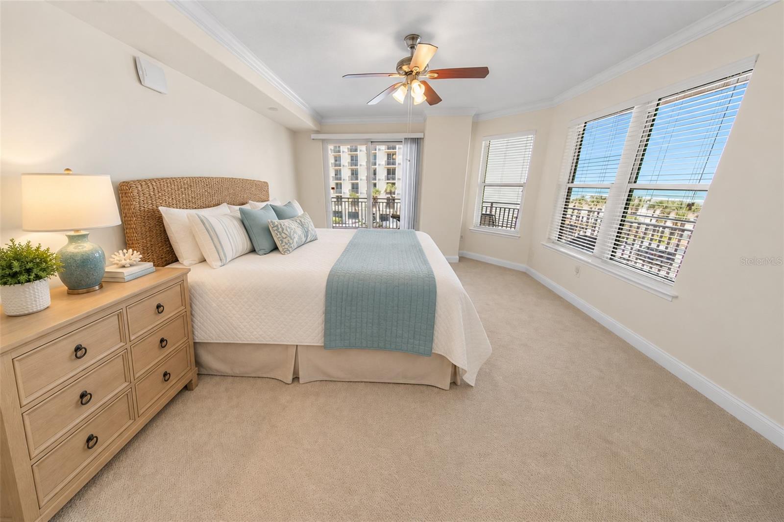 Staged bedroom with a woven-headboard bed and ocean glimpses through large windows.