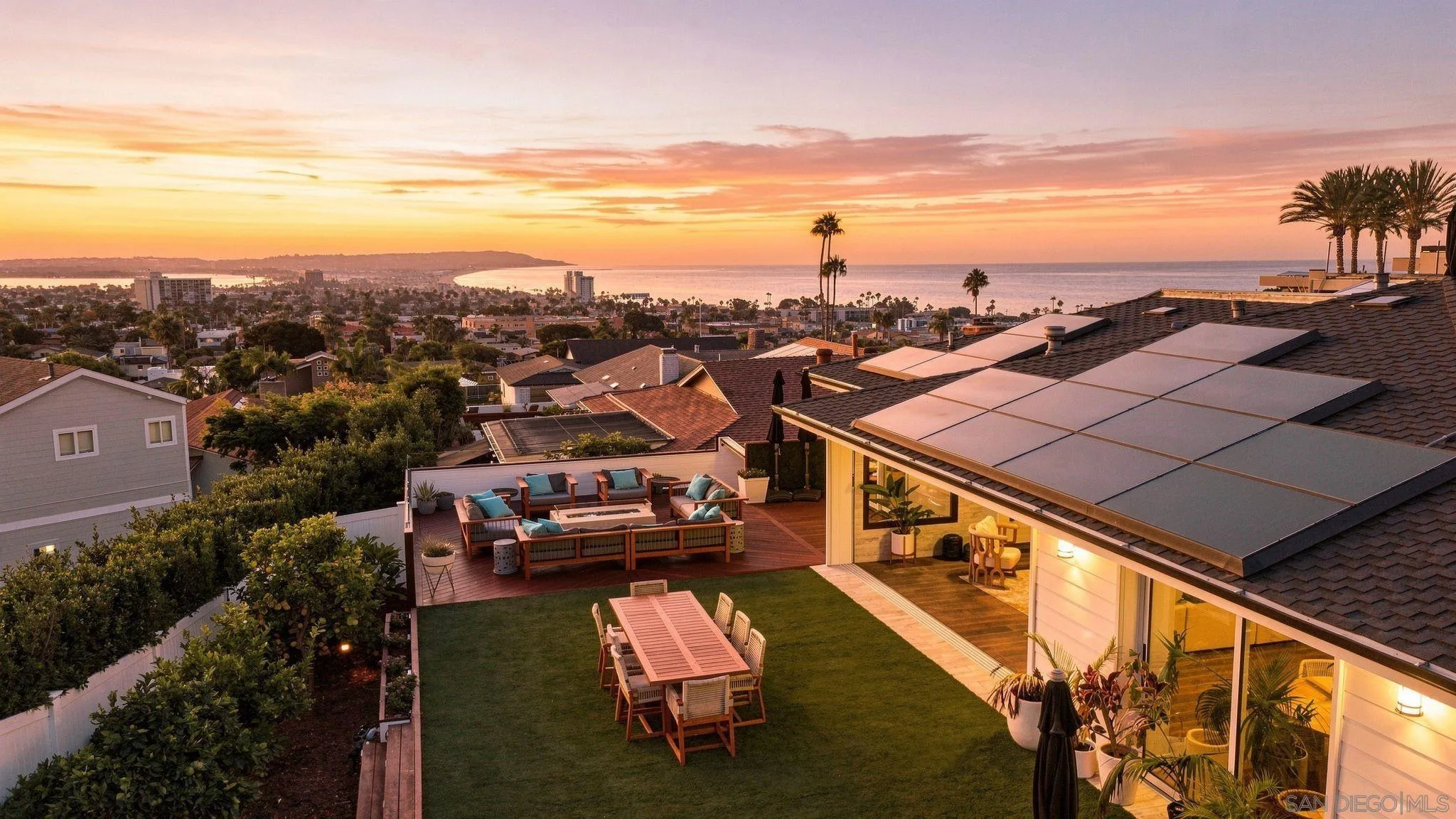 Rooftop deck with outdoor seating and lawn overlooking the ocean at sunset.
