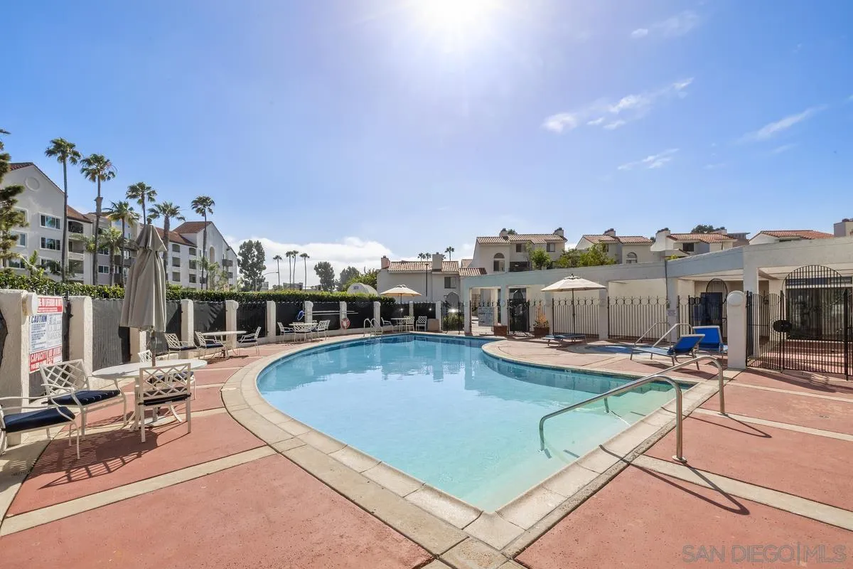 Residential complex pool with lounge chairs, umbrellas, and apartment buildings.