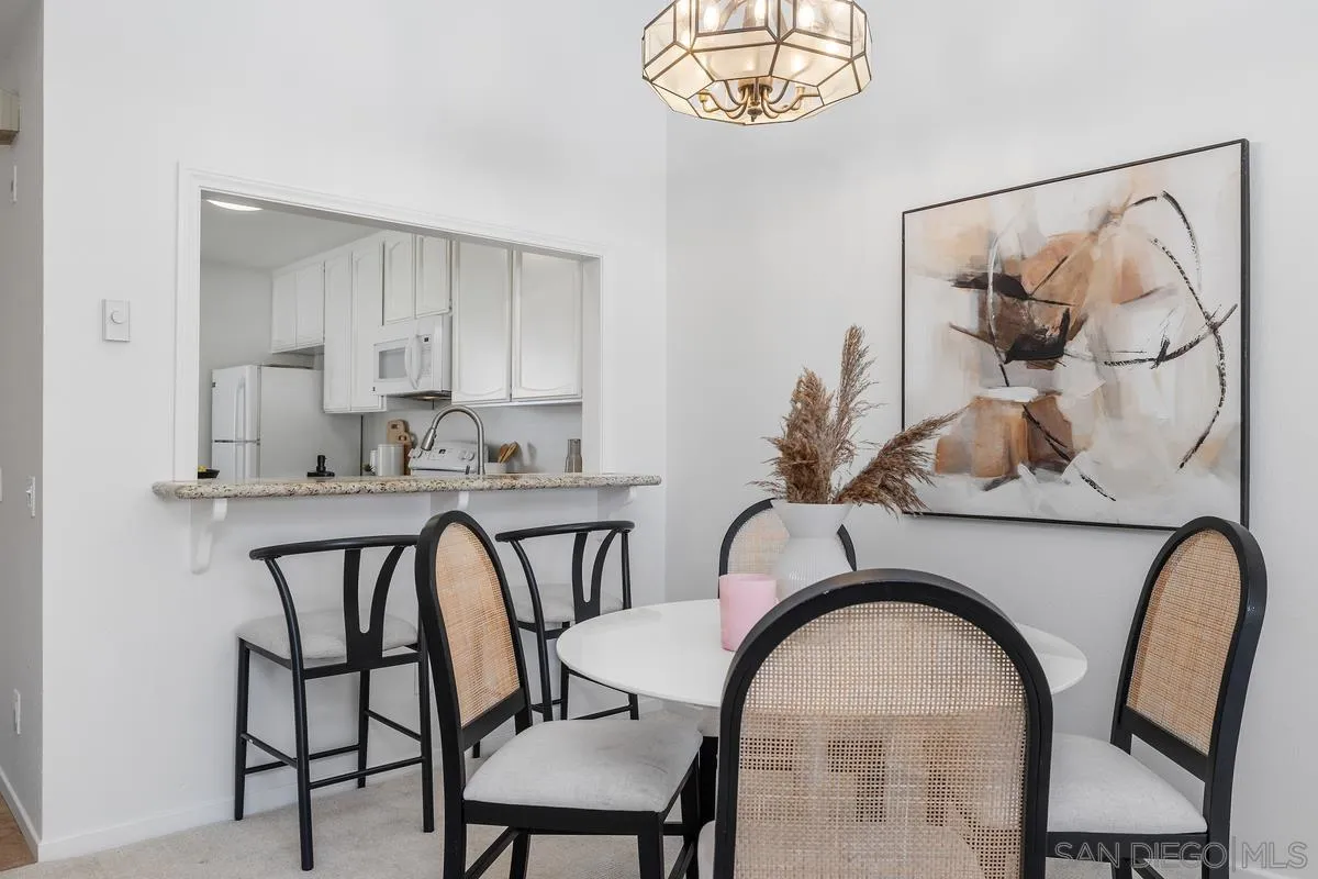 Dining area with a round white table, cane-back chairs, and a kitchen pass-through.