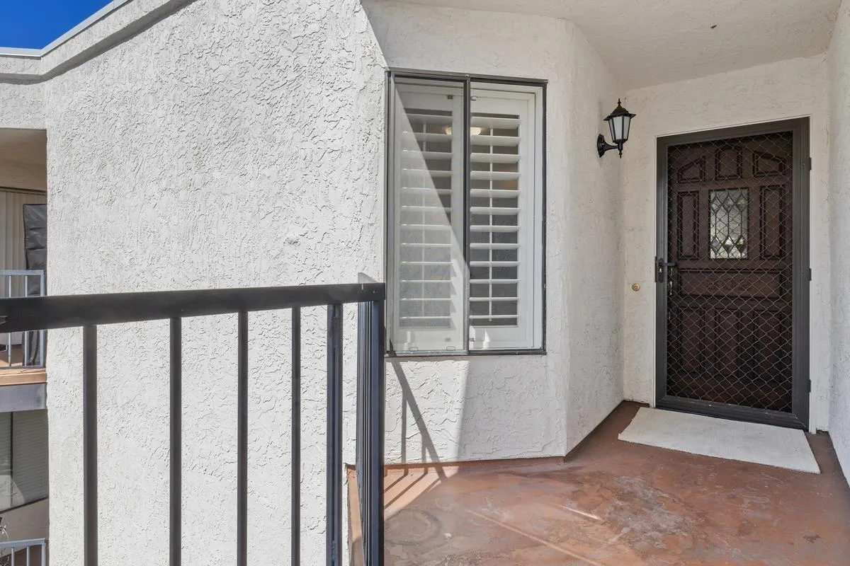 Condominium balcony with a black railing, shuttered window, and screened entry door.