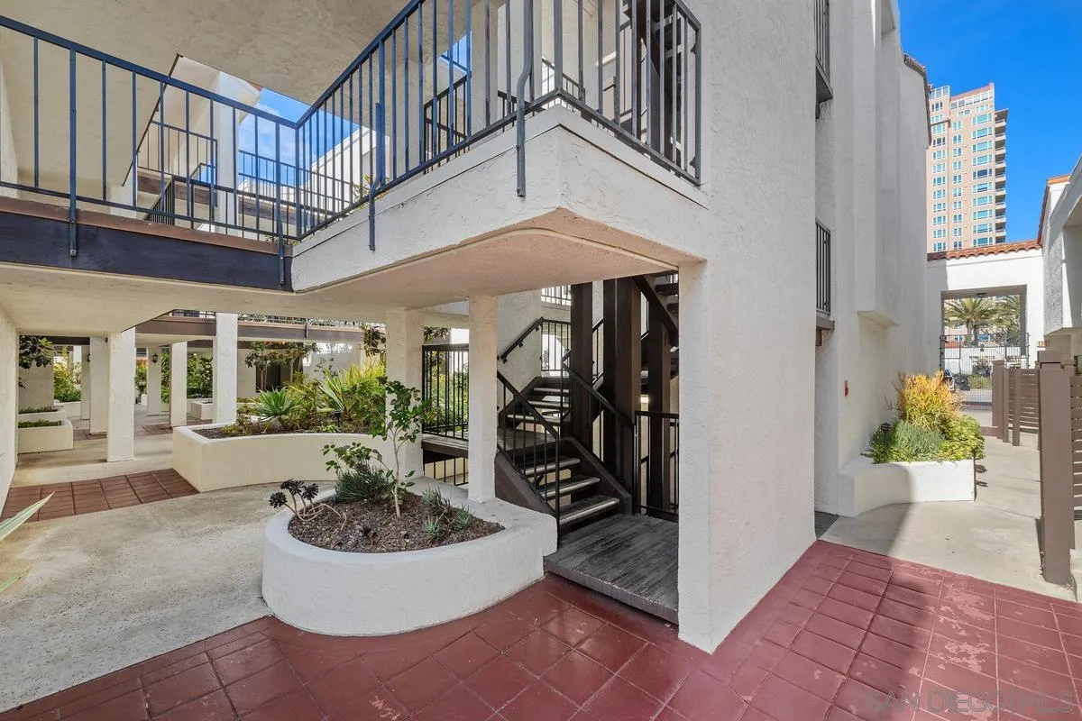 Apartment courtyard with exterior stairs, metal-railed balconies, raised planters, and red tile paving.