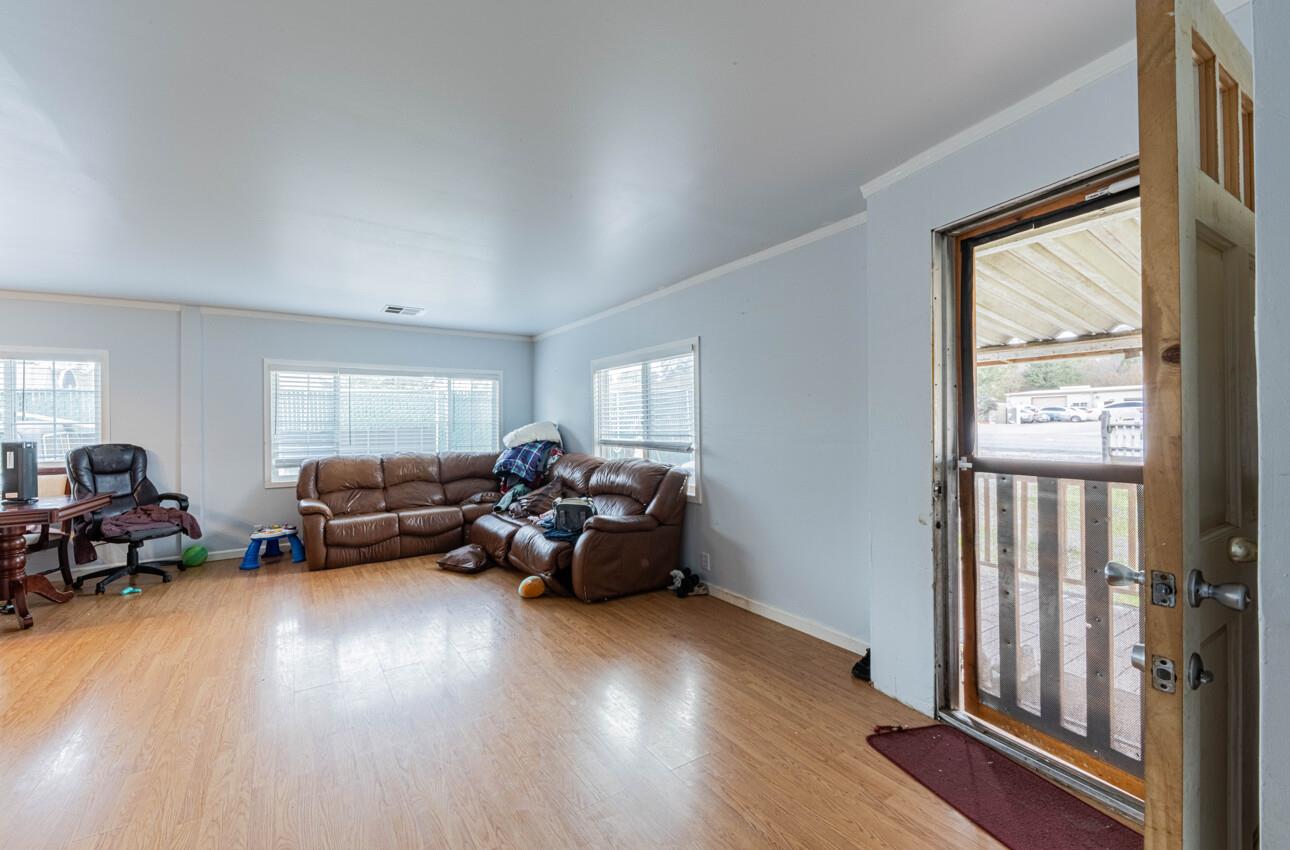 Living room with brown leather sectional, light wood flooring, and an open door to a covered porch.