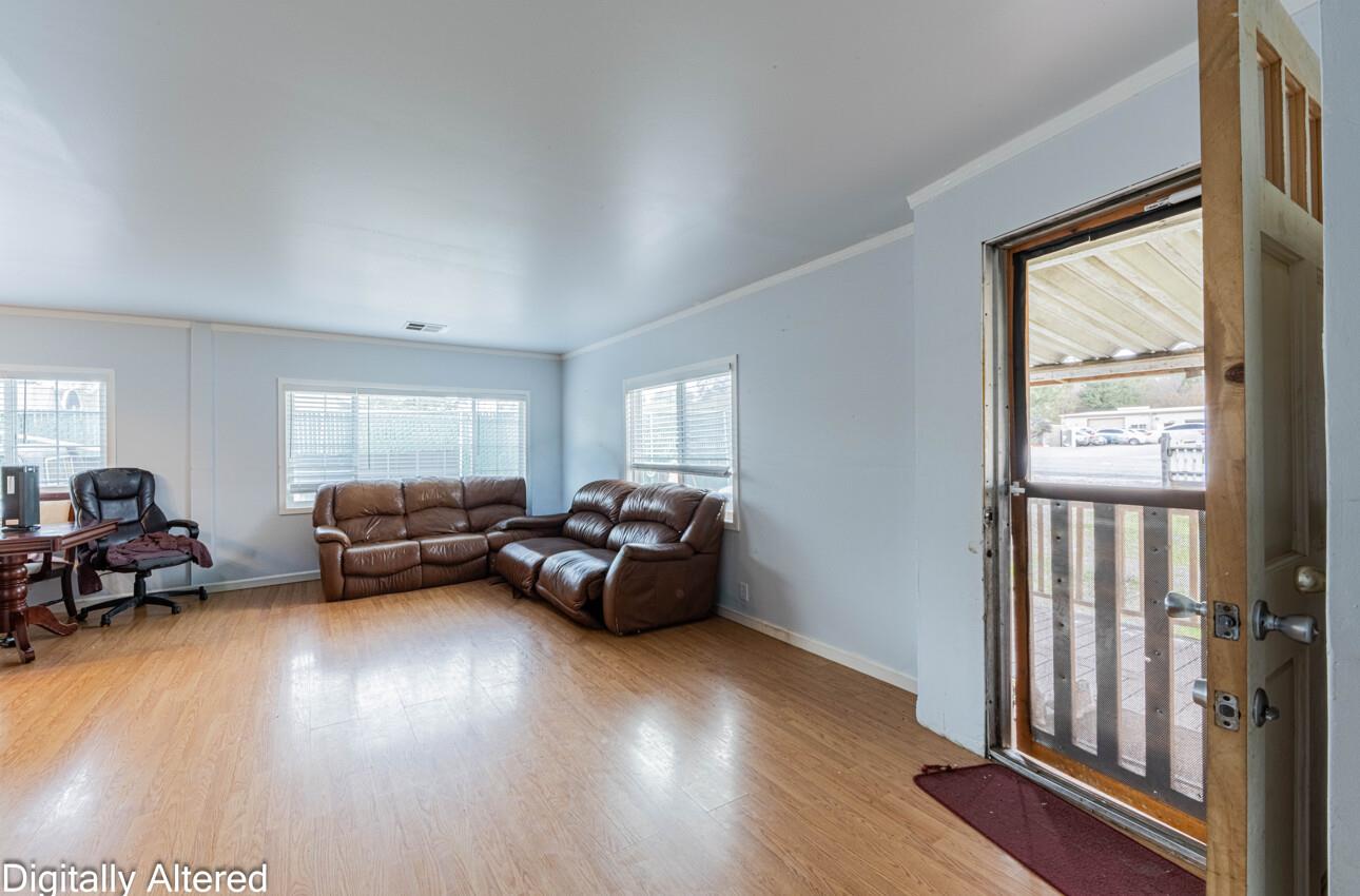 Living room with a brown leather sectional, light wood floors, and an open door to a covered porch.