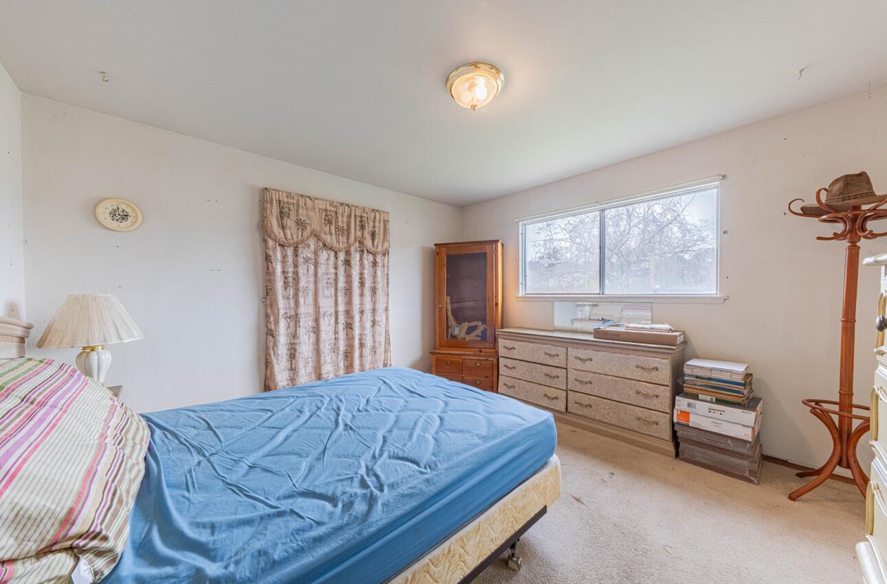 Bedroom with a blue-covered bed, floral curtains, and dressers beneath a wide window.