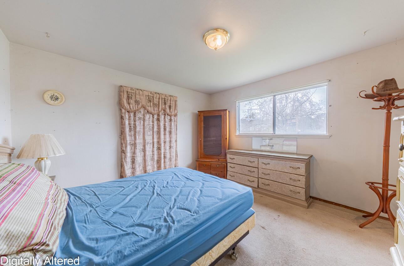 Bedroom with a blue-covered bed, patterned curtains, and wooden dressers.