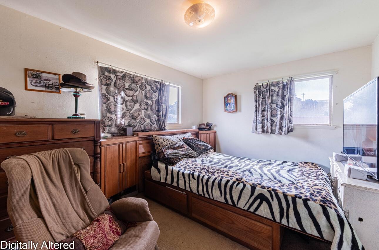 Bedroom with patterned bedding, wood cabinetry, a recliner, and two curtained windows.