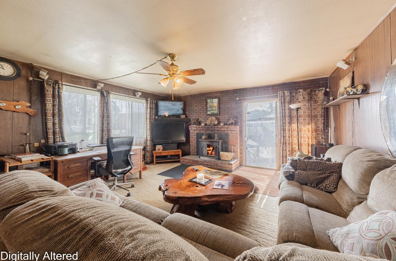 Living room with a brick fireplace, wood-burning stove, sofas, and large sunlit windows.