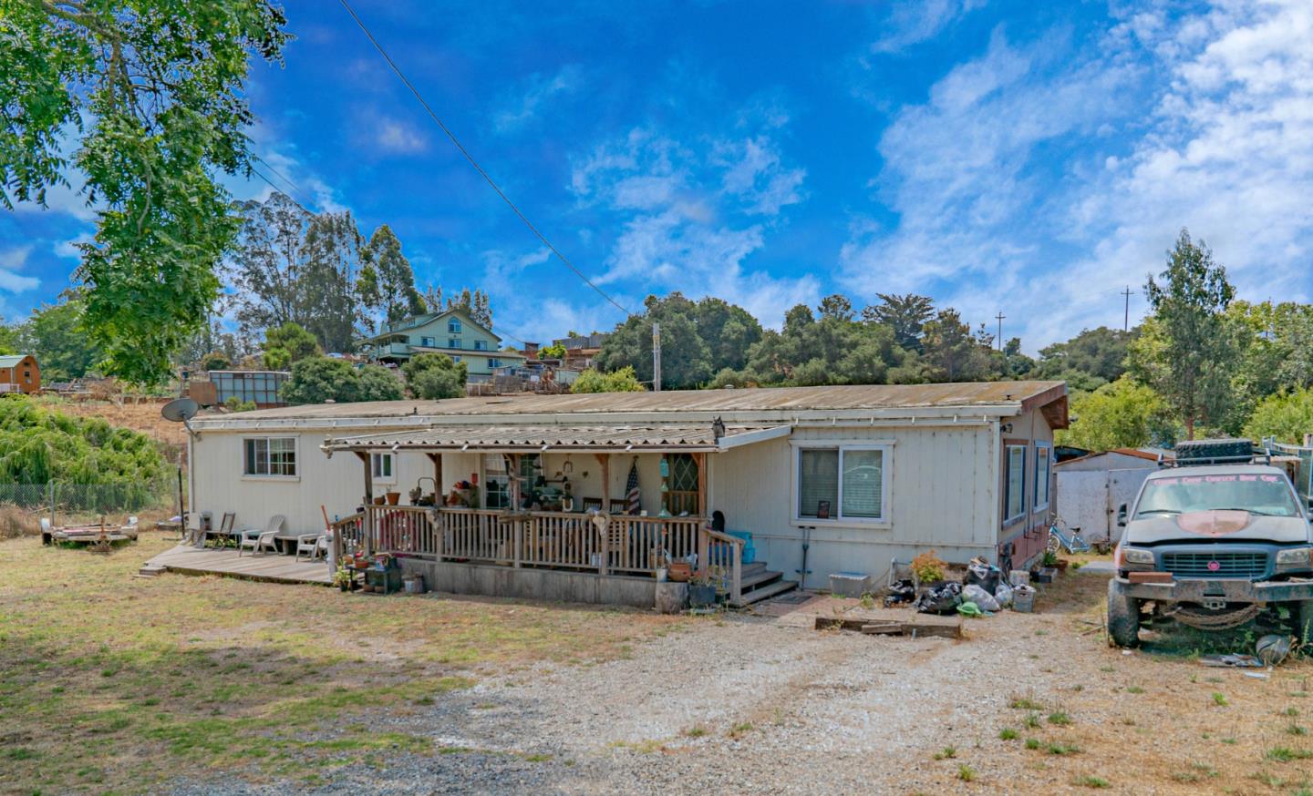 Single-story manufactured home with a covered porch and deck on a dry lot beside a pickup truck.