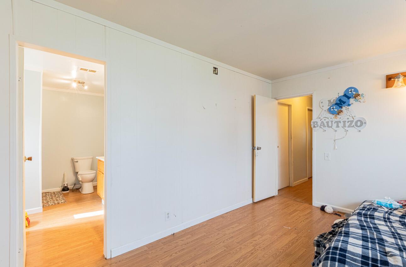 Bedroom with light wood flooring, paneled walls, and an open doorway to a bathroom.