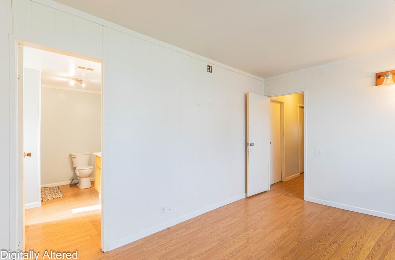 Empty room with wood flooring, white paneled walls, and open doorways to a bathroom and hall.