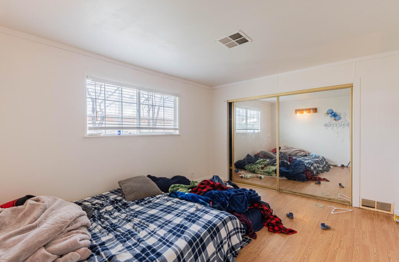 Bedroom with rumpled blue plaid bedding, mirrored closet doors, and belongings scattered on the floor.