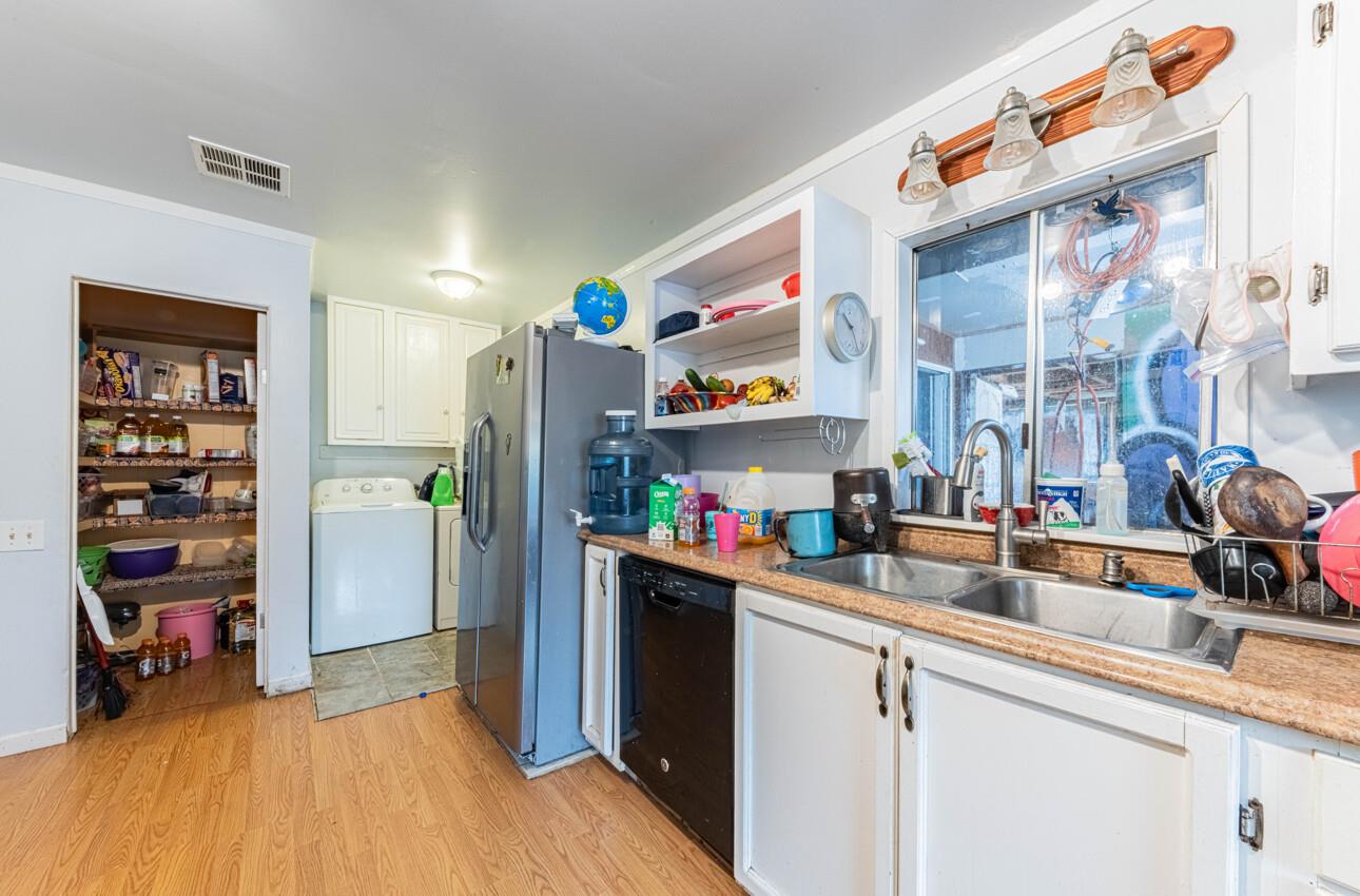 Kitchen with a stocked open pantry, stainless-steel refrigerator, and double-basin sink beneath a window.
