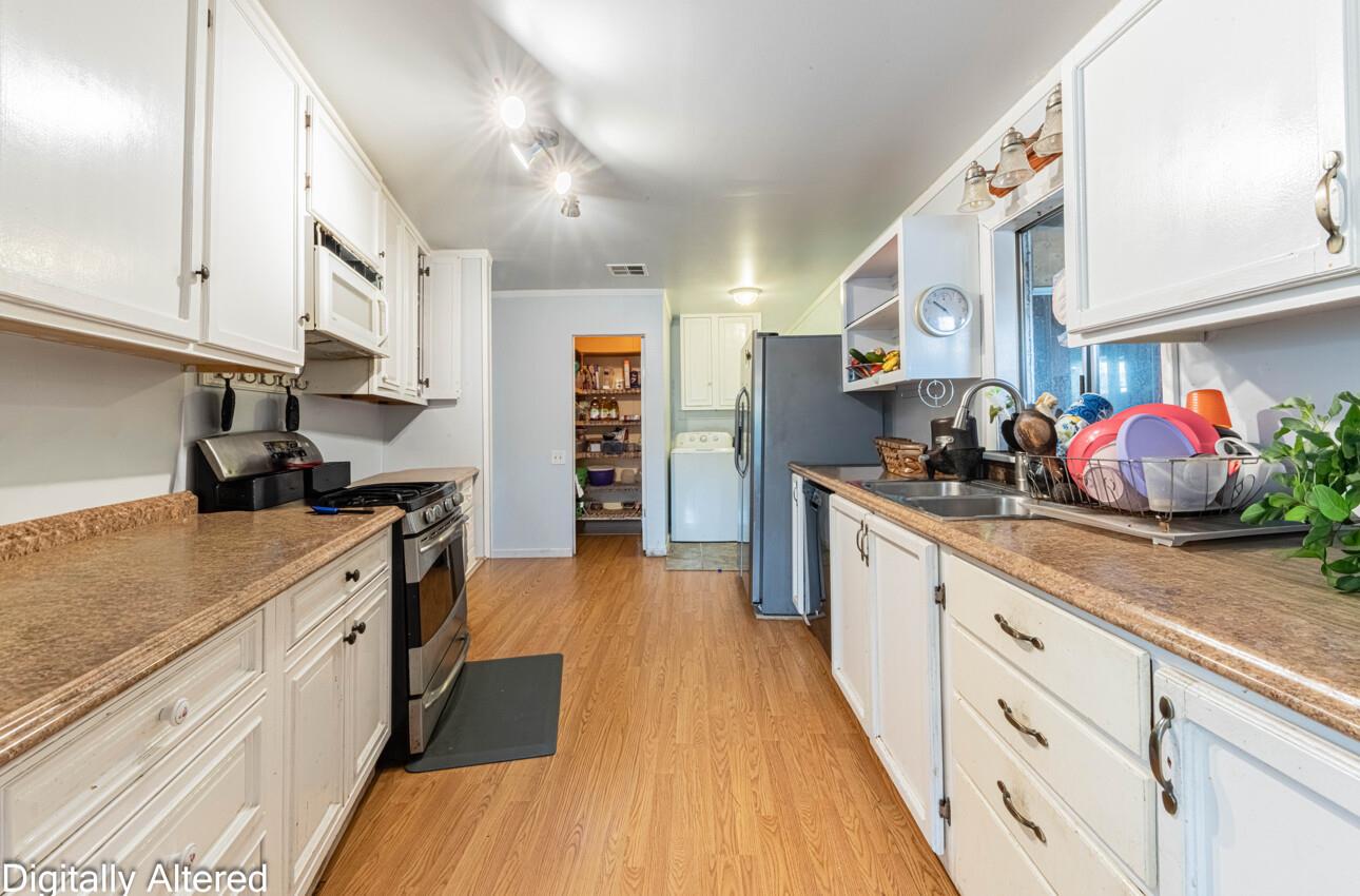 Kitchen with white cabinetry, brown countertops, stainless-steel appliances, and wood flooring.