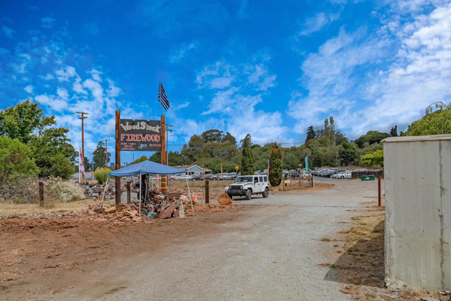 Firewood business yard with a Woodstock Firewood sign, blue canopy, and parked vehicles.