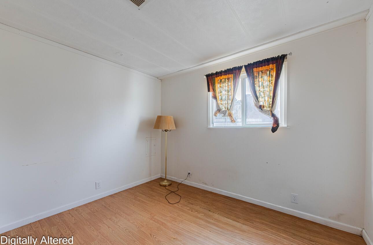 Empty room with light wood flooring, a curtained window, and a brass floor lamp.