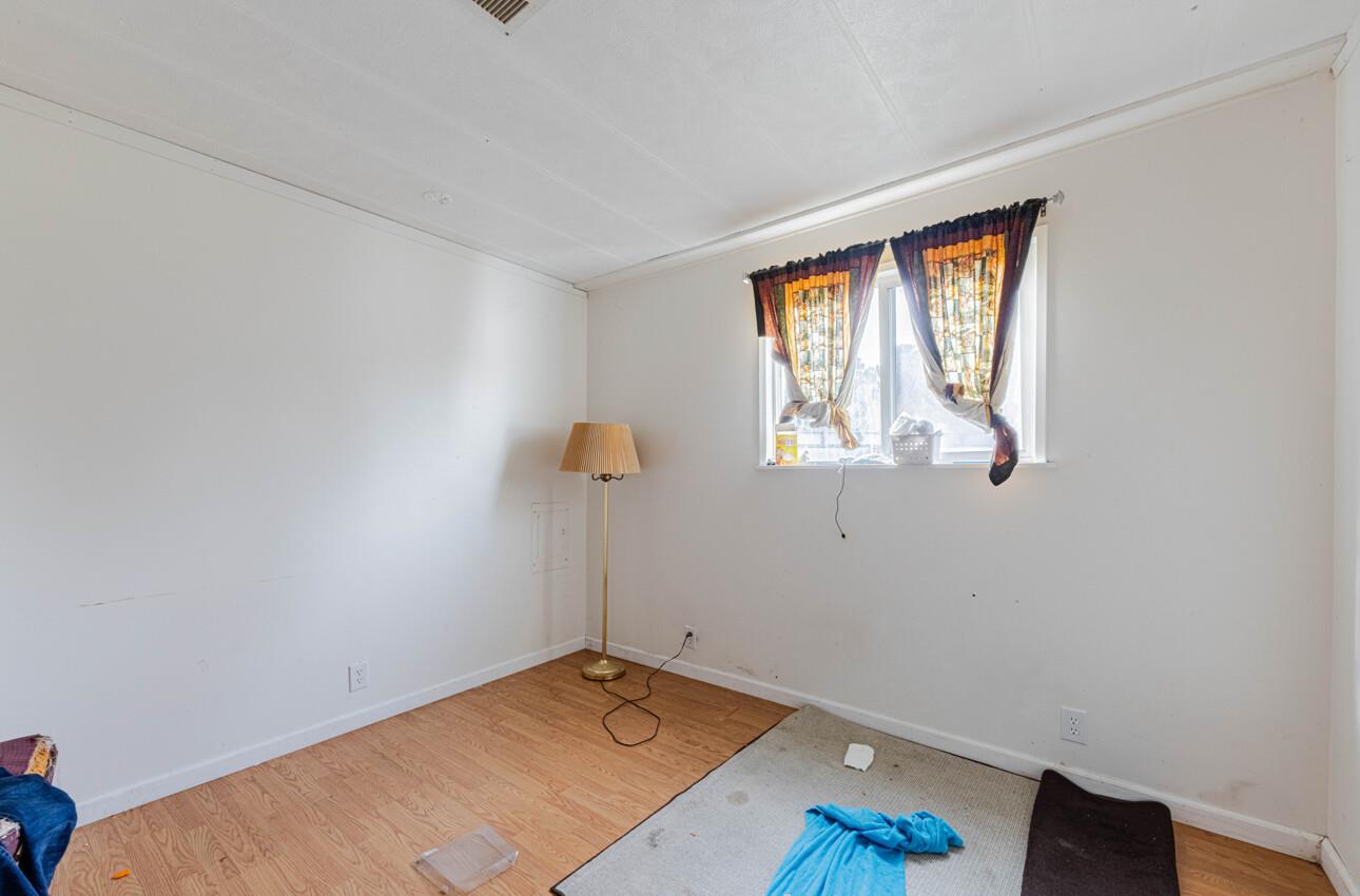 Sparsely furnished room with a curtained window, wood-look flooring, and a floor lamp.