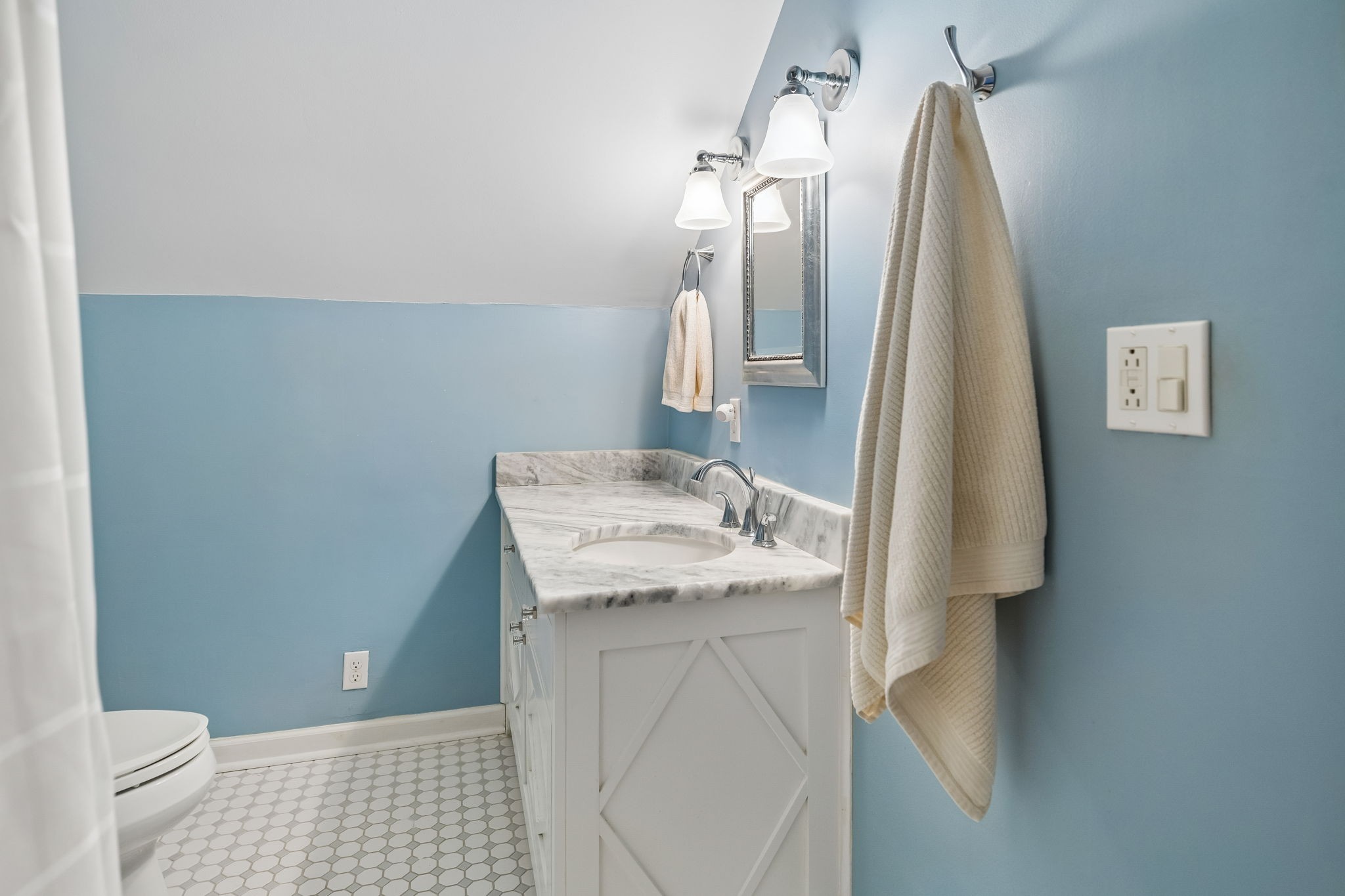 Bathroom with a marble-topped white vanity, blue walls, and hexagonal tile floor.