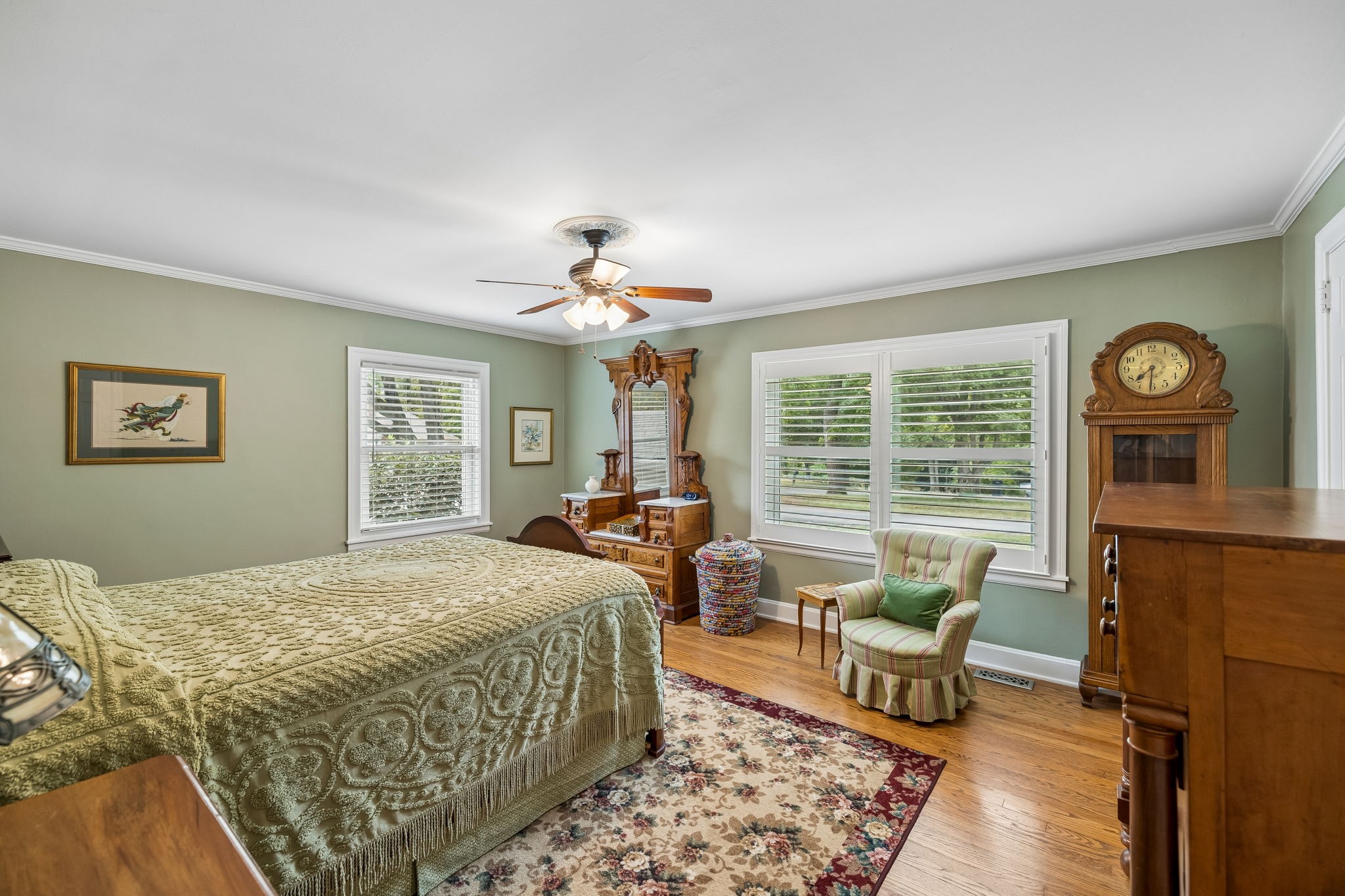 Furnished bedroom with sage walls, carved wooden furniture, shuttered windows, and a floral rug.