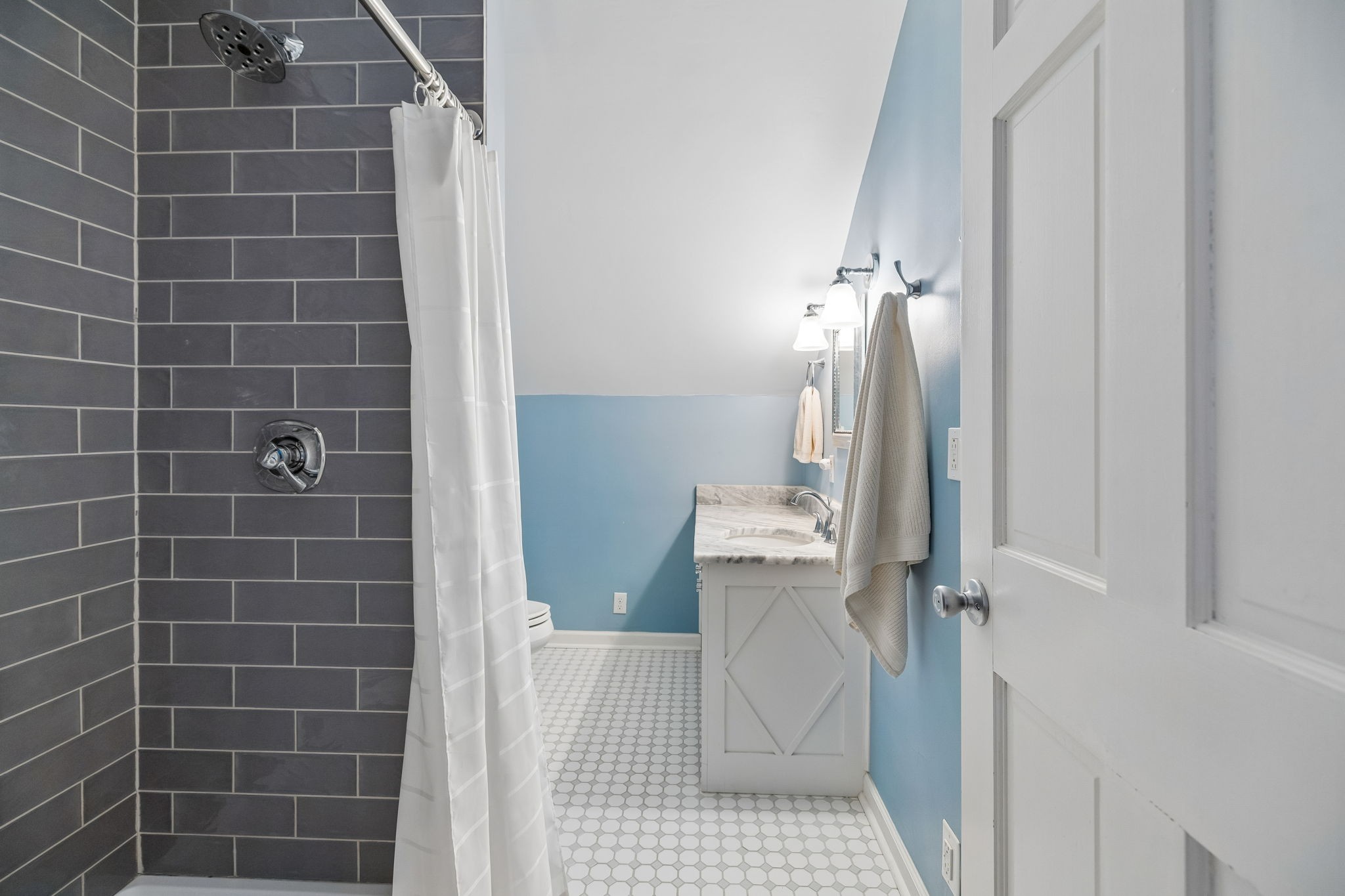 Bathroom with a charcoal-tile shower, blue walls, marble-topped vanity, and white hexagonal floor tile.
