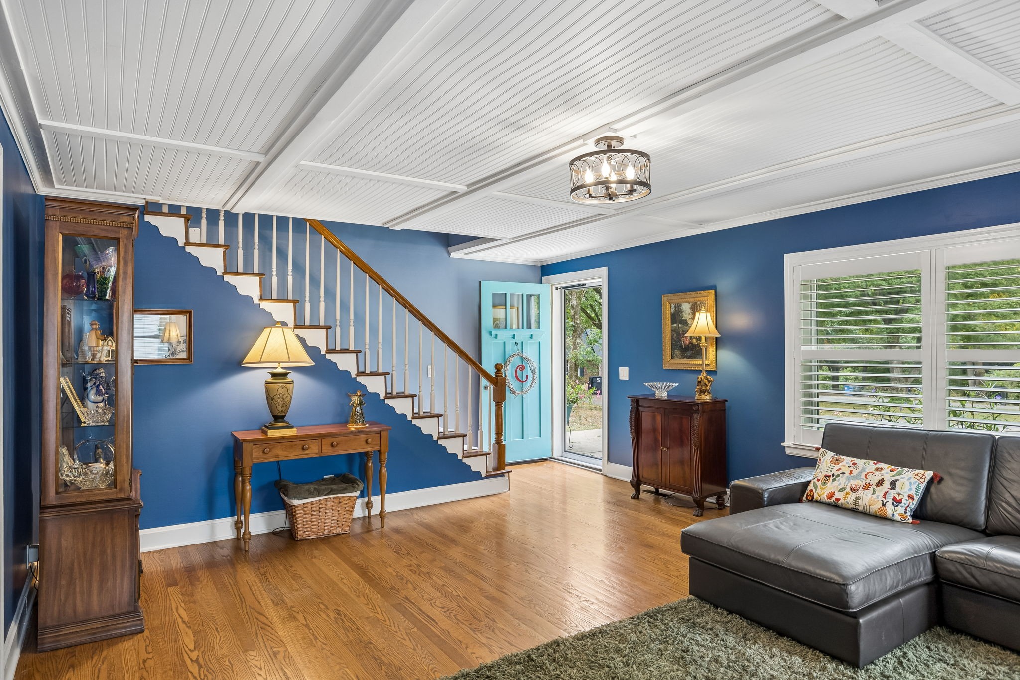 Living room with blue walls, hardwood floors, a white staircase, and an open turquoise front door.