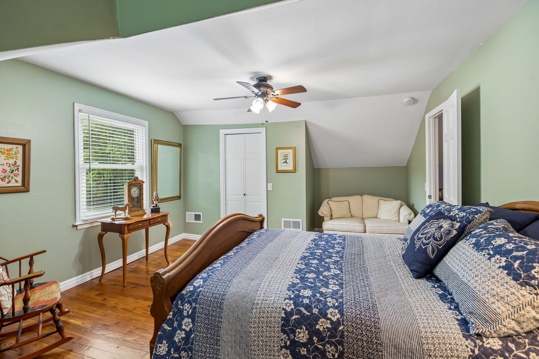 Bedroom with blue patterned bedding, hardwood floors, pale green walls, and a cozy sitting area.