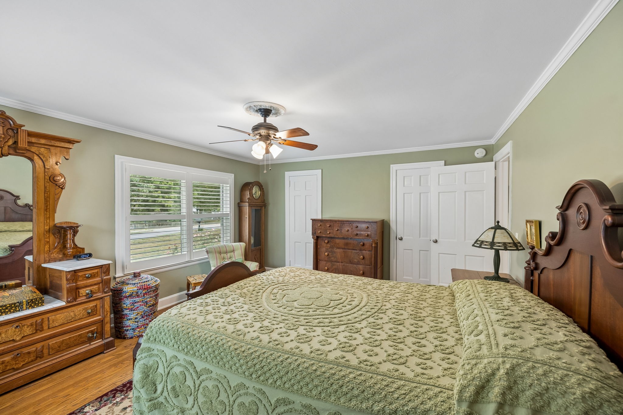 Furnished bedroom with a pale green quilt, antique wooden furniture, and shuttered windows.