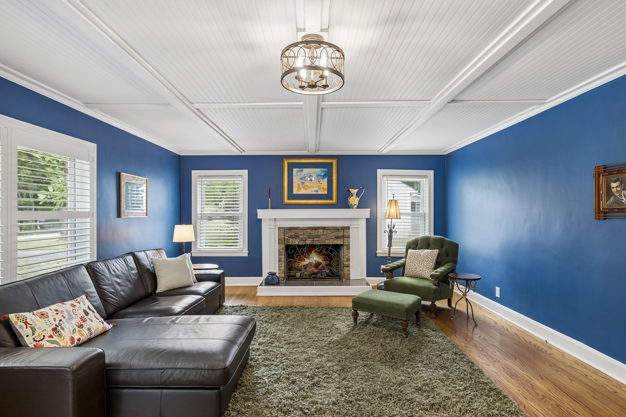 Blue living room with a white paneled ceiling, fireplace, leather sectional, and green armchair.