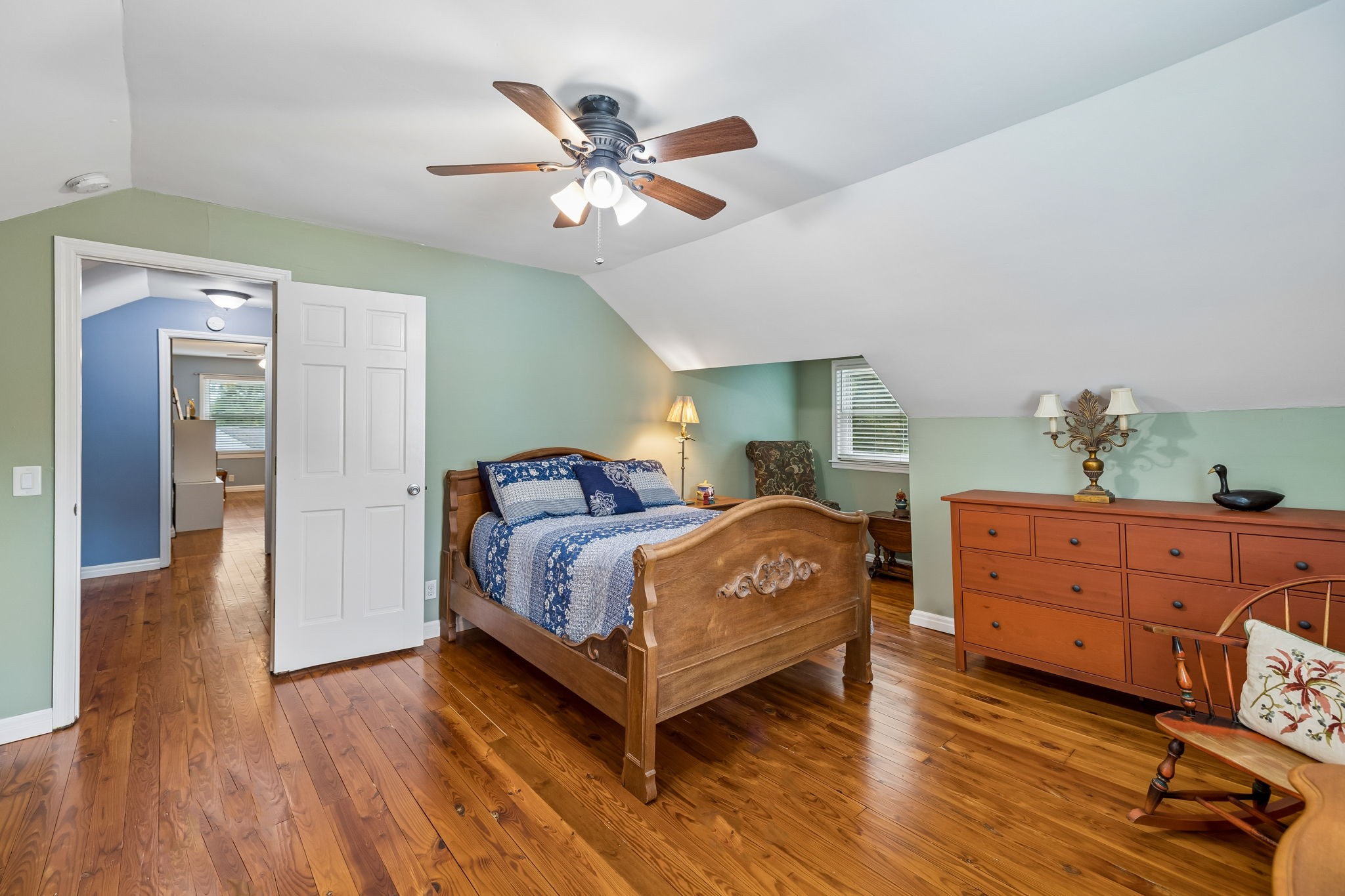 Attic bedroom with carved wooden bed, blue bedding, green walls, and polished hardwood floors.
