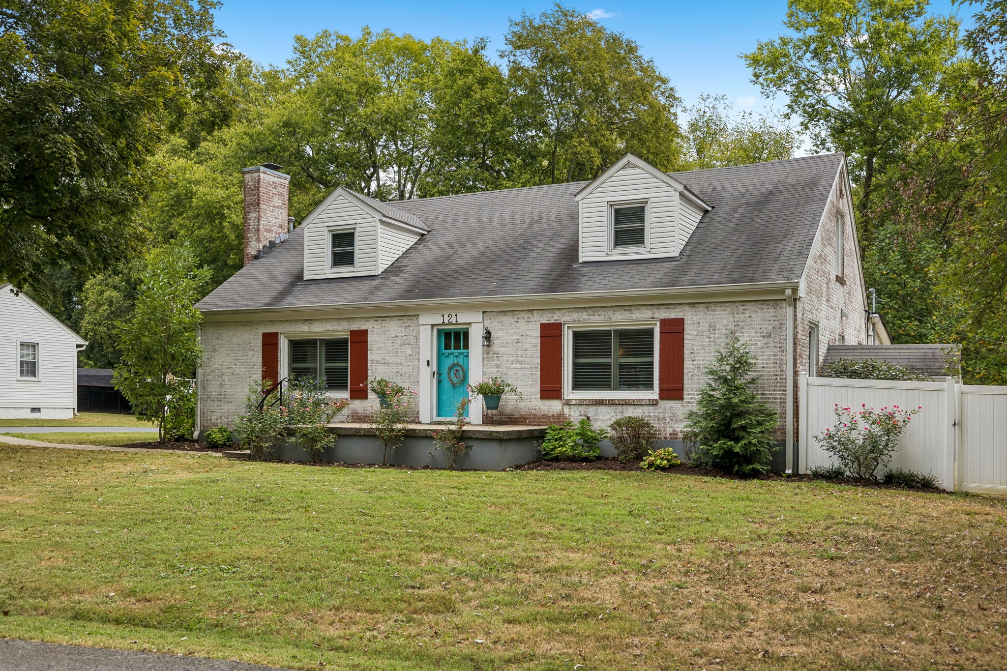 Light brick house with two dormers, red shutters, and a turquoise front door.