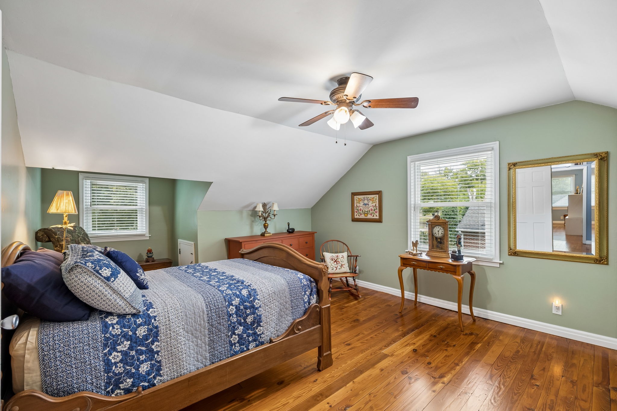 Bedroom with a wooden bed, blue-and-white bedding, sage green walls, and hardwood floors.