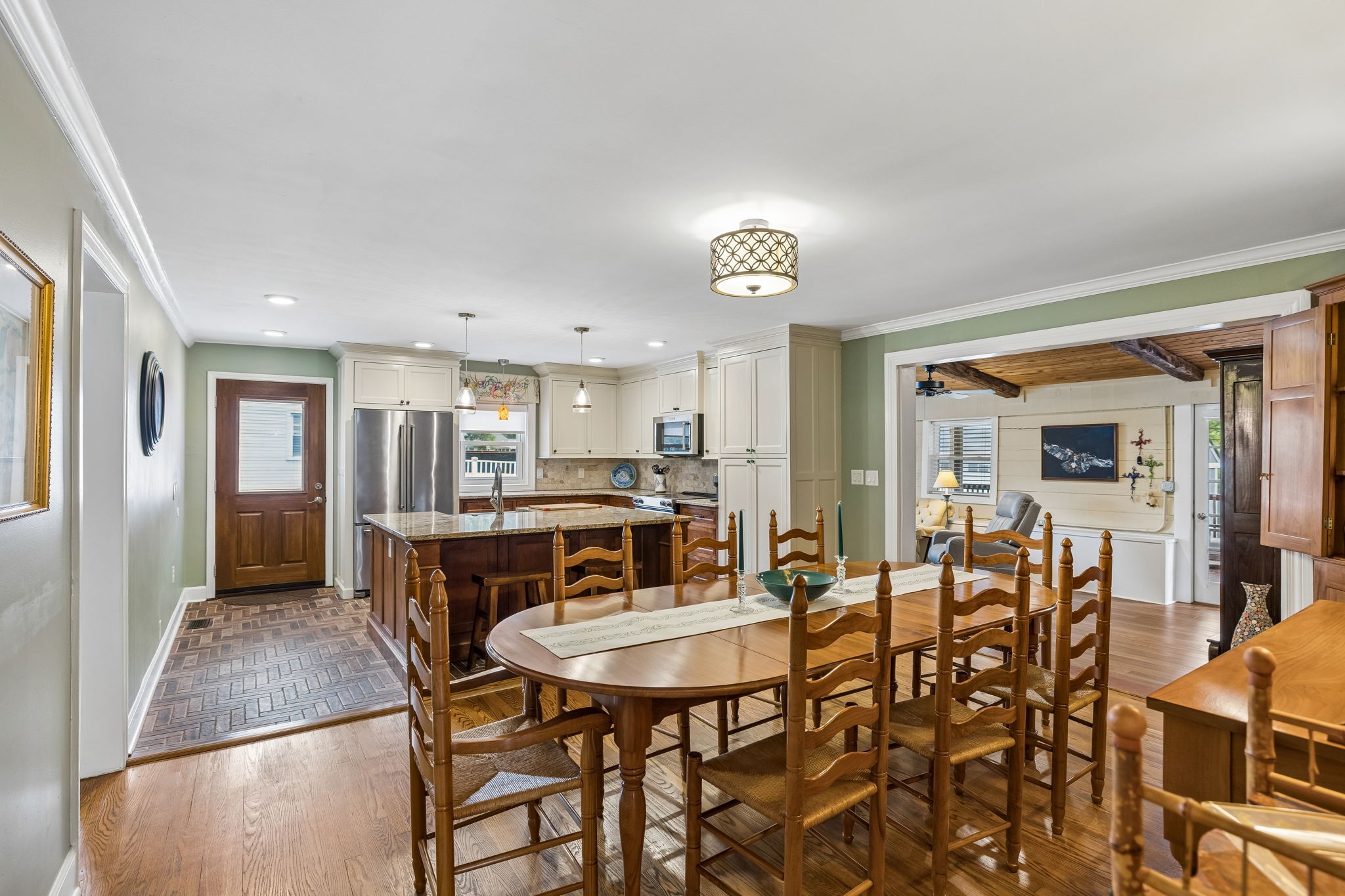 Dining room and kitchen with a large wooden table, stone-topped island, white cabinets, and stainless steel appliances.