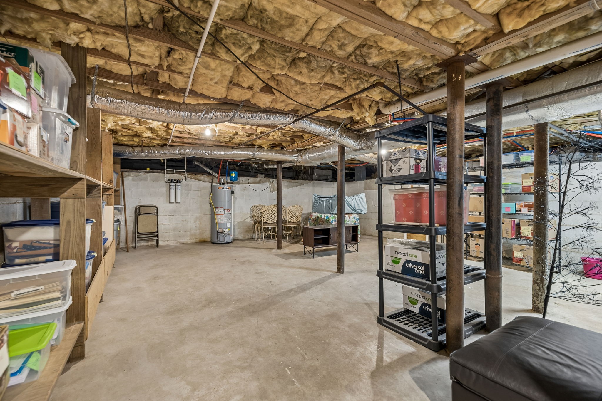 Unfinished basement with exposed insulation, storage shelving, a water heater, and metal support posts.