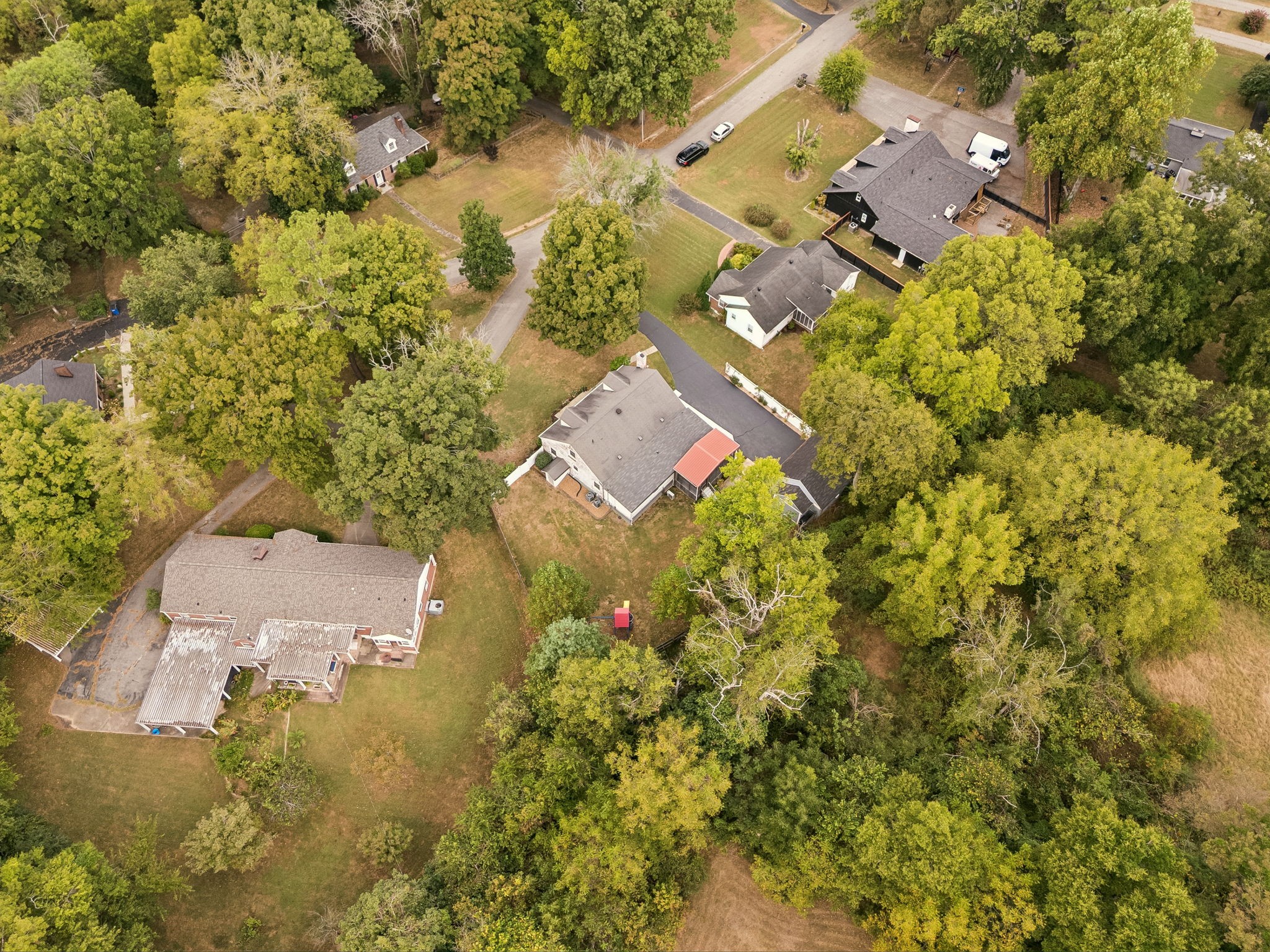 Aerial view of a gray-roofed home with a red awning among mature trees and neighboring houses.