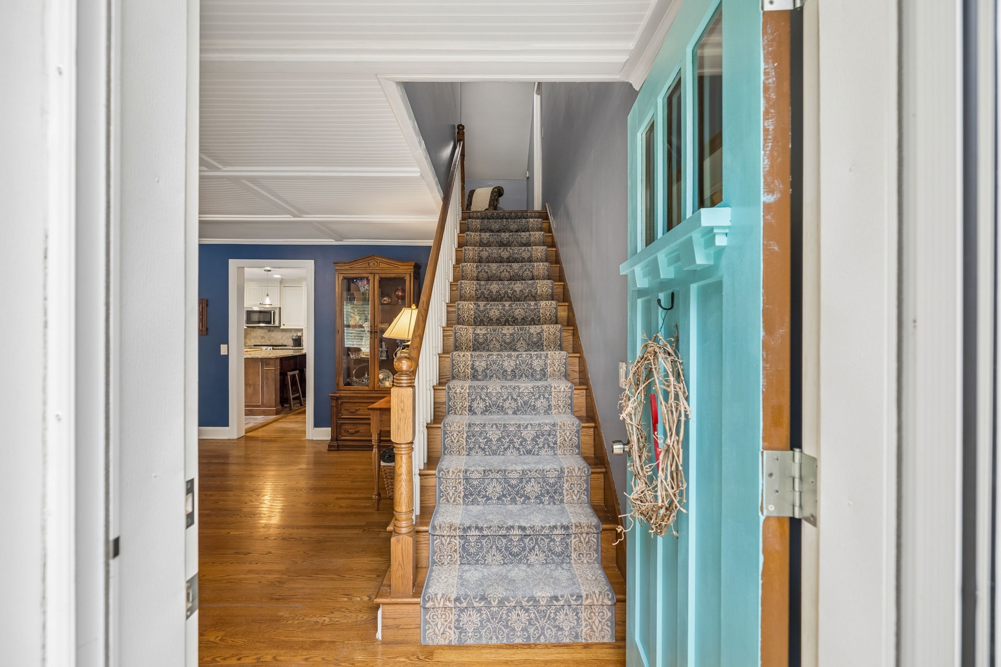 Entry hall with a patterned staircase runner, hardwood floors, and an open turquoise front door.