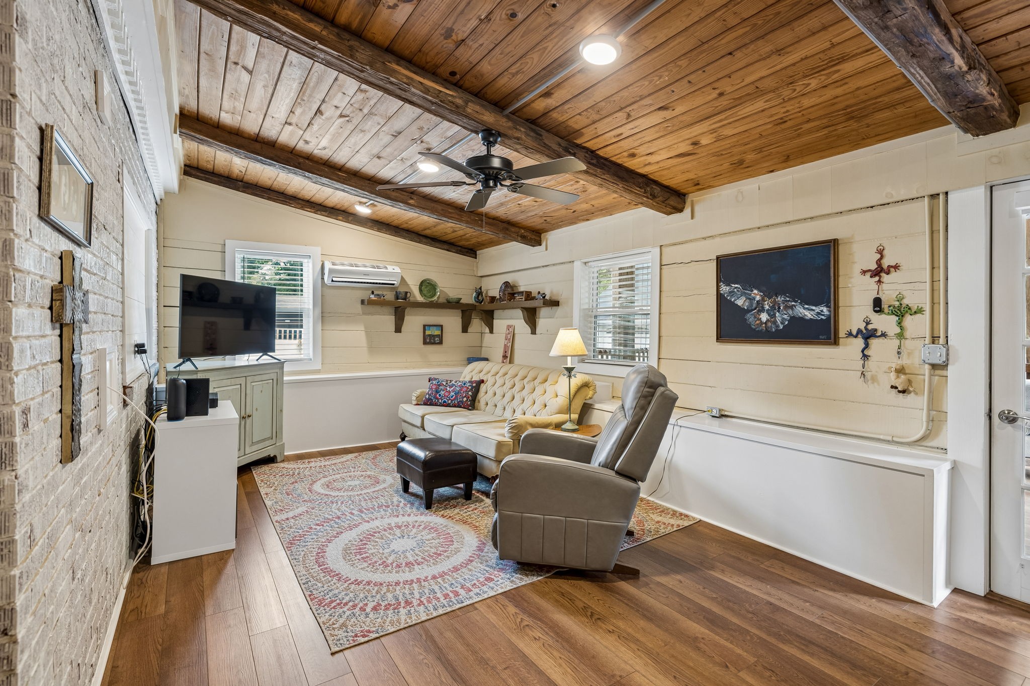 Living room with a vaulted wood ceiling, exposed beams, cream sofa, and patterned rug.