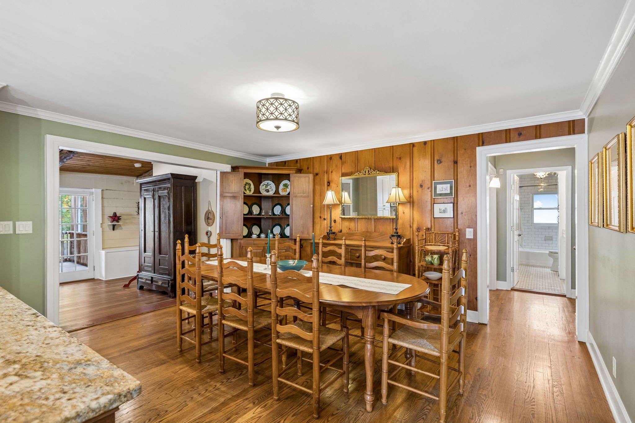 Dining room with a long wooden table, ladder-back chairs, and warm wood-paneled walls.