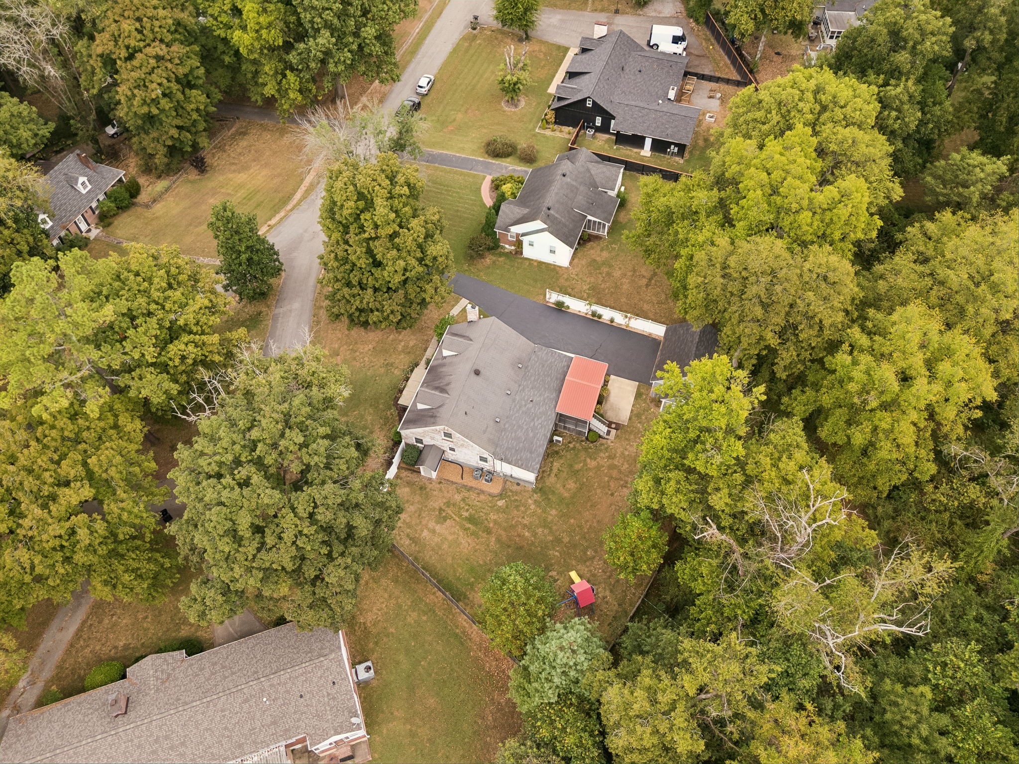 Aerial view of a house with a fenced yard, red-roofed patio cover, and surrounding trees.